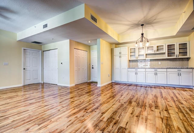 kitchen featuring decorative backsplash, light stone counters, decorative light fixtures, light hardwood / wood-style floors, and white cabinetry