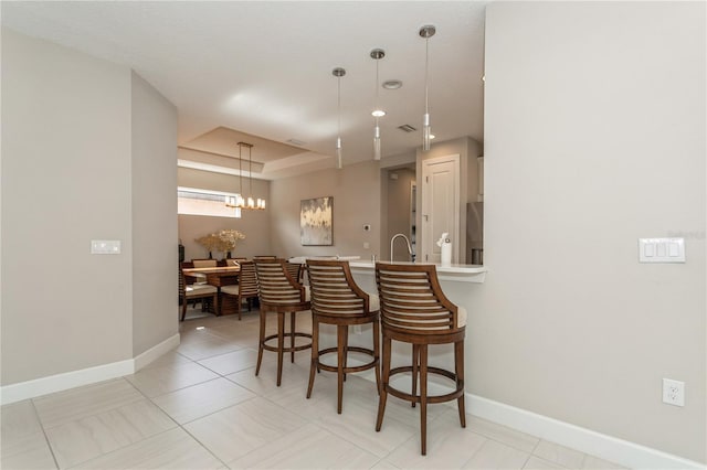 kitchen featuring a chandelier, decorative light fixtures, a raised ceiling, light tile patterned floors, and a breakfast bar area