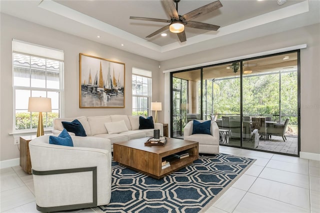 living room featuring a raised ceiling, ceiling fan, and light tile patterned floors