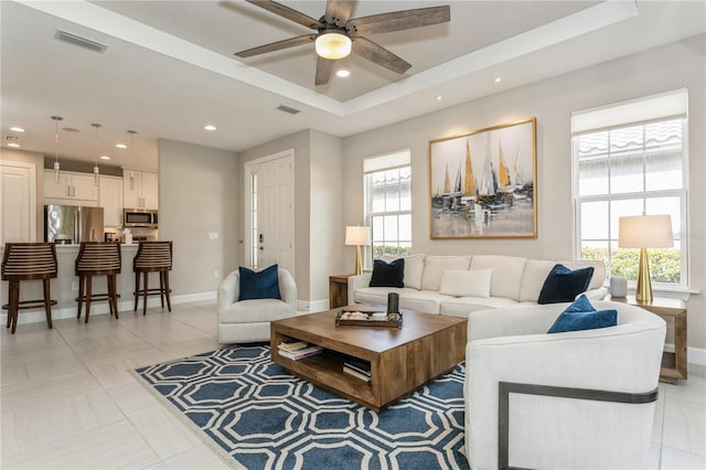 tiled living room with ceiling fan and a tray ceiling