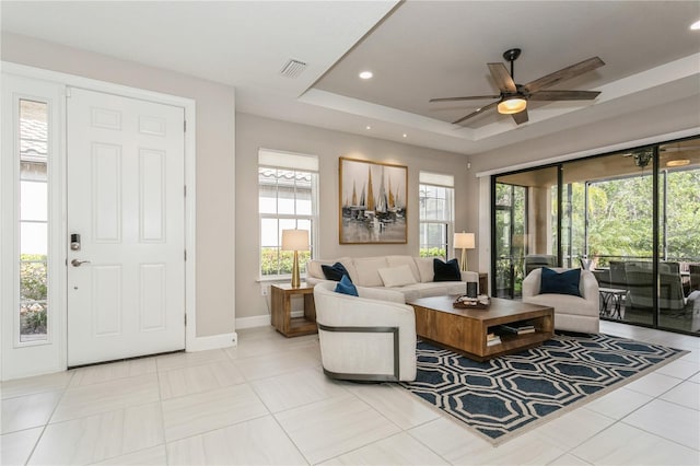 tiled living room featuring ceiling fan, a tray ceiling, and a healthy amount of sunlight