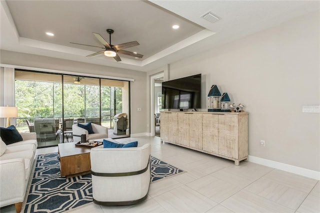 tiled living room with ceiling fan and a tray ceiling