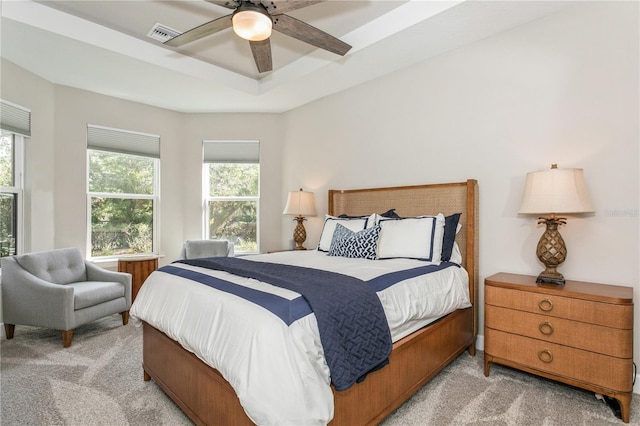 carpeted bedroom with ceiling fan and a raised ceiling