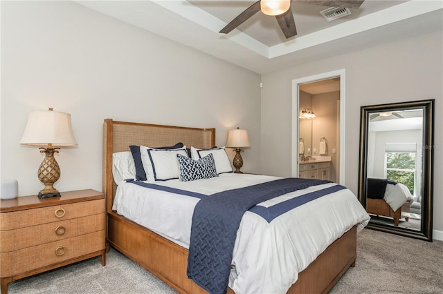 carpeted bedroom with ceiling fan, ensuite bathroom, and a raised ceiling