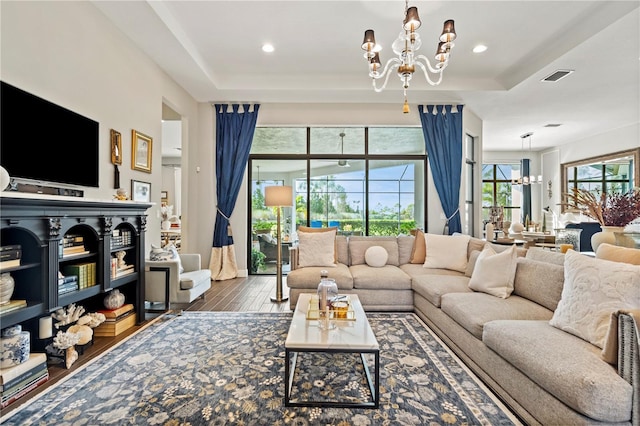 living room with a raised ceiling, hardwood / wood-style flooring, and an inviting chandelier