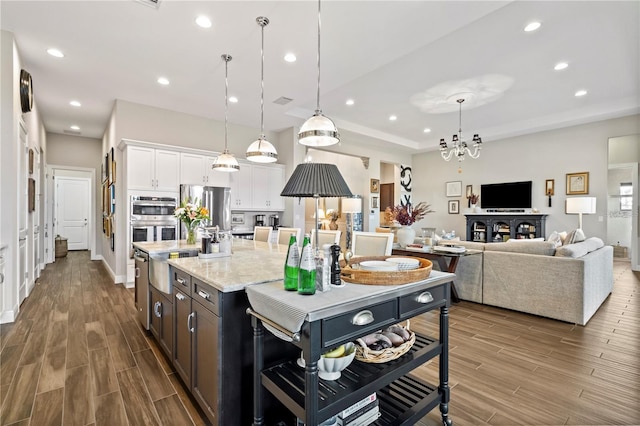 kitchen with white cabinetry, stainless steel appliances, an inviting chandelier, decorative light fixtures, and a center island with sink