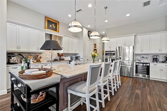 kitchen featuring white cabinets, stainless steel appliances, beverage cooler, and hanging light fixtures