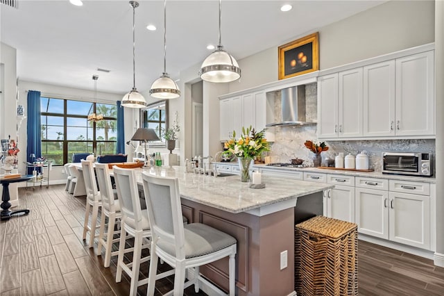 kitchen with tasteful backsplash, white cabinetry, a breakfast bar, and wall chimney range hood