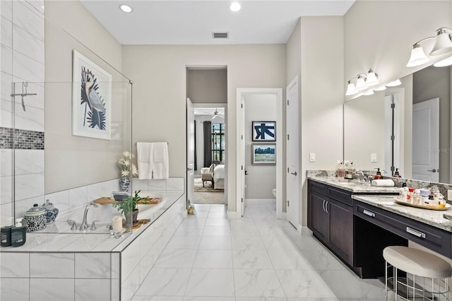 bathroom featuring vanity, ceiling fan, a relaxing tiled tub, and toilet