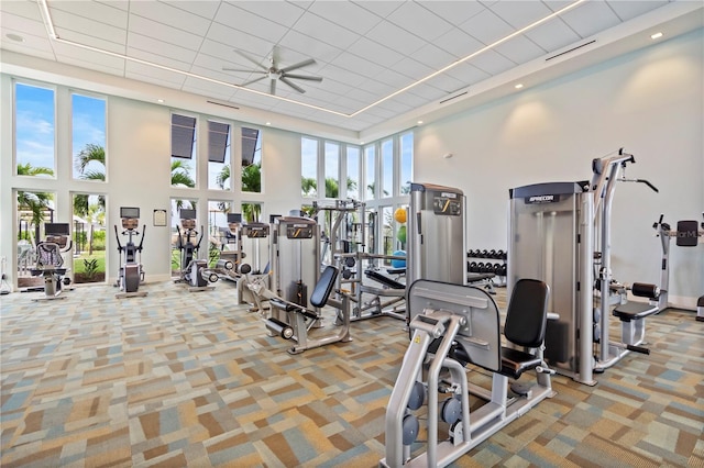 gym featuring ceiling fan, a wealth of natural light, light colored carpet, and a high ceiling