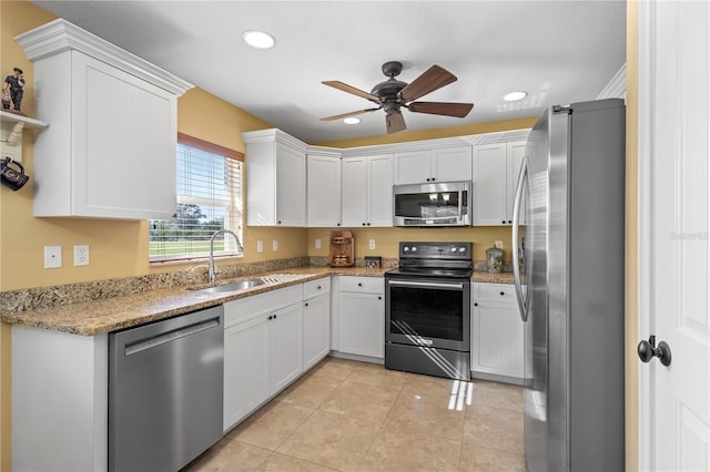 kitchen with light stone countertops, stainless steel appliances, ceiling fan, sink, and white cabinets