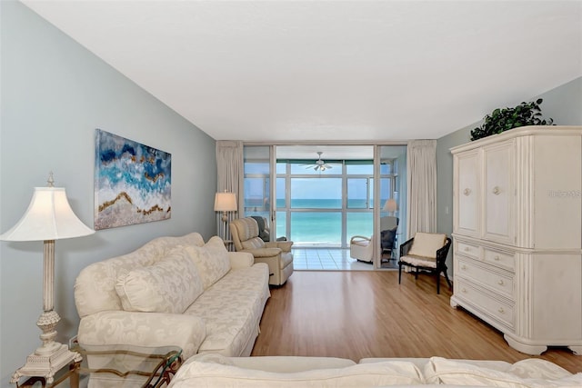 living room featuring ceiling fan, a water view, light wood-type flooring, and a wall of windows