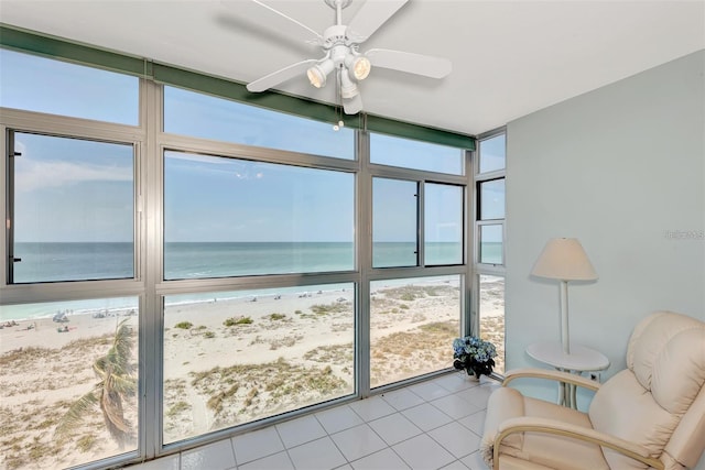 unfurnished sunroom with ceiling fan, a water view, and a view of the beach