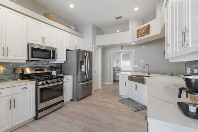 kitchen with light stone countertops, appliances with stainless steel finishes, white cabinetry, and sink