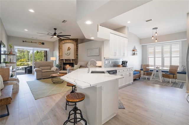 kitchen featuring white cabinets, sink, hanging light fixtures, light stone counters, and a kitchen bar