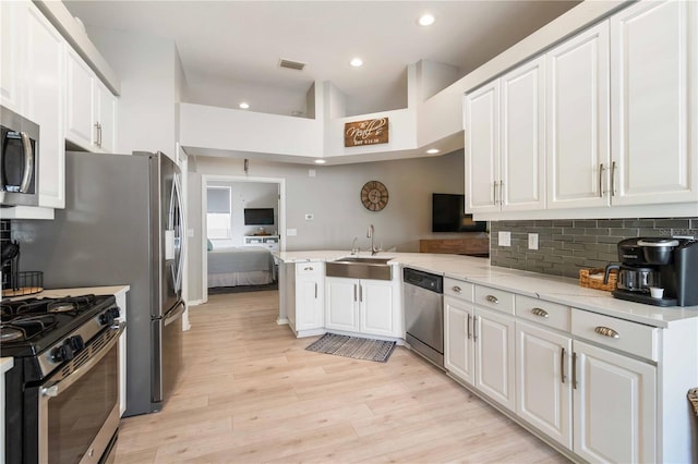 kitchen with kitchen peninsula, appliances with stainless steel finishes, sink, light hardwood / wood-style flooring, and white cabinets