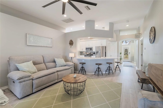 living room with ceiling fan, light hardwood / wood-style floors, and a towering ceiling