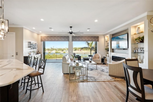 living room featuring ceiling fan, built in shelves, crown molding, and light hardwood / wood-style flooring