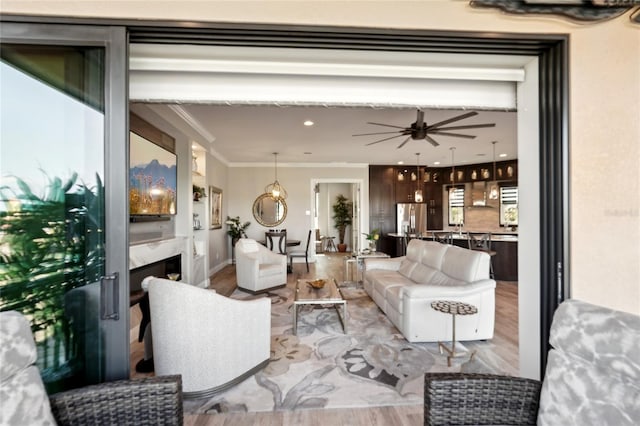 living room featuring ceiling fan, light wood-type flooring, a fireplace, and ornamental molding