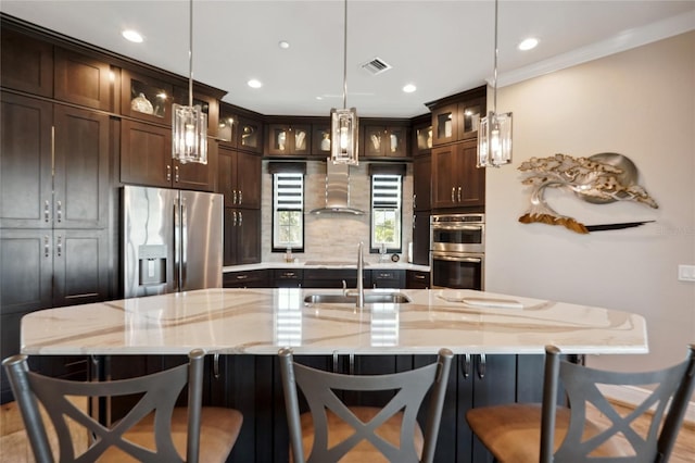 kitchen with a large island with sink, pendant lighting, stainless steel appliances, sink, and light stone counters