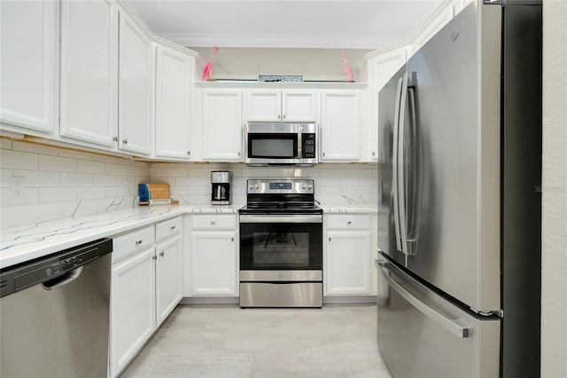 kitchen featuring light stone countertops, appliances with stainless steel finishes, tasteful backsplash, light tile patterned floors, and white cabinetry