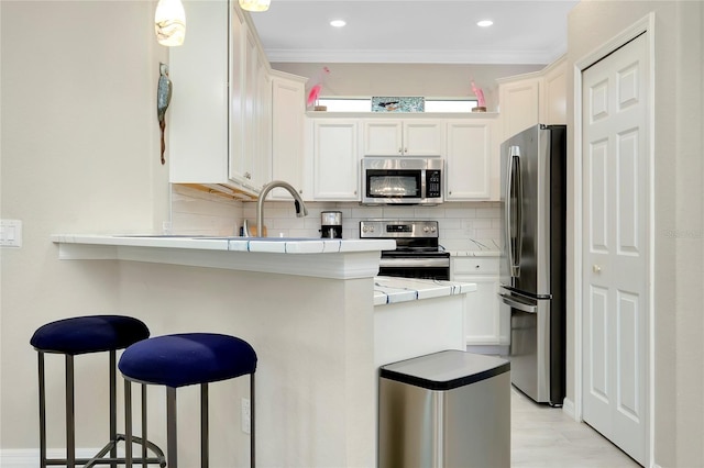 kitchen with white cabinetry, backsplash, a breakfast bar area, appliances with stainless steel finishes, and ornamental molding