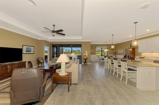 living room featuring a raised ceiling, ceiling fan, sink, and ornamental molding