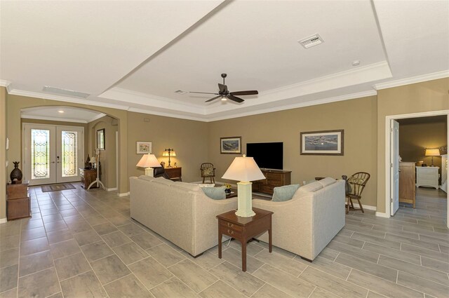 living room with ceiling fan, ornamental molding, a tray ceiling, and french doors