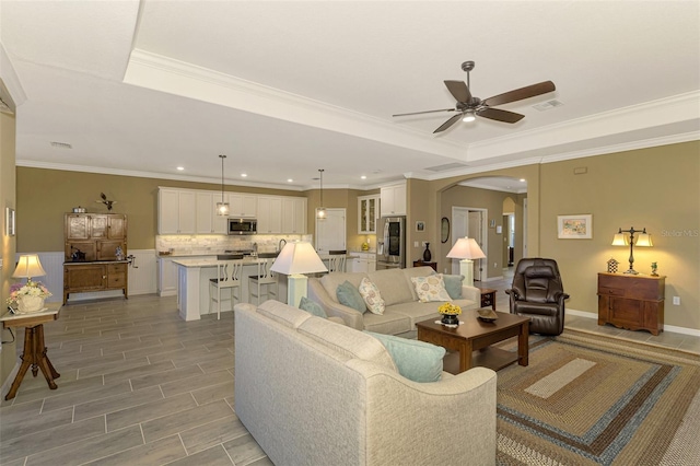 living room with a raised ceiling, ceiling fan, and ornamental molding