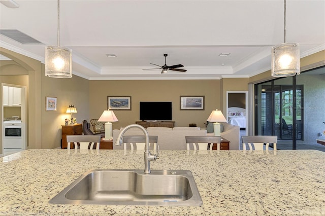 kitchen with ornamental molding, ceiling fan, sink, washer / clothes dryer, and hanging light fixtures