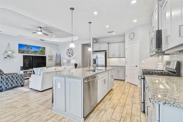 kitchen featuring wood finish floors, open floor plan, stainless steel appliances, a ceiling fan, and a sink