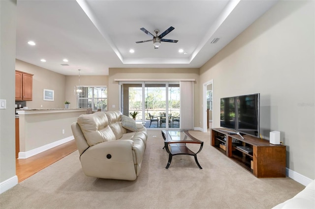 living room with ceiling fan, light colored carpet, and a tray ceiling