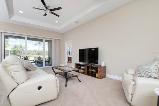 living room with a raised ceiling, light colored carpet, and ceiling fan