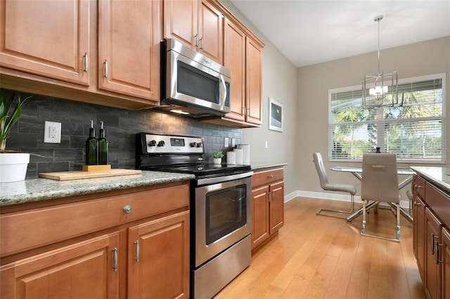 kitchen with light wood-type flooring, backsplash, hanging light fixtures, light stone countertops, and appliances with stainless steel finishes