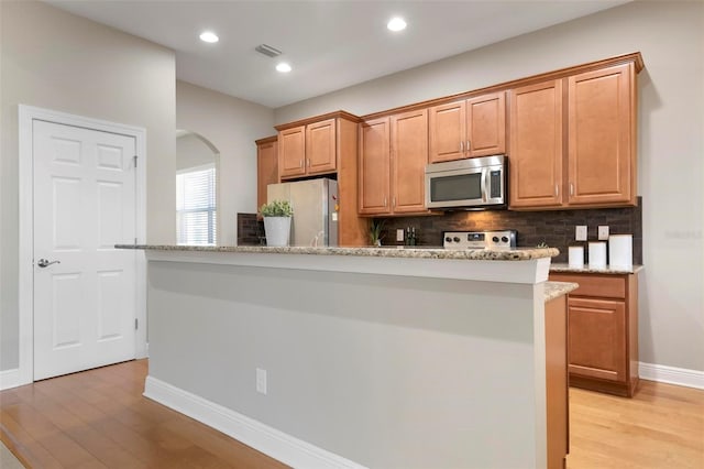 kitchen with appliances with stainless steel finishes, tasteful backsplash, a center island, and light stone countertops