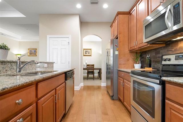 kitchen with light stone countertops, appliances with stainless steel finishes, light hardwood / wood-style flooring, and sink