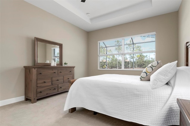 bedroom with a raised ceiling, ceiling fan, and light carpet