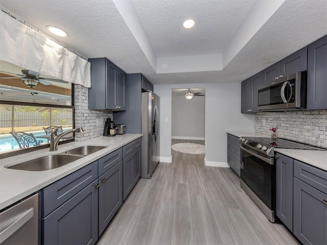 kitchen with sink, light hardwood / wood-style flooring, a textured ceiling, gray cabinets, and appliances with stainless steel finishes