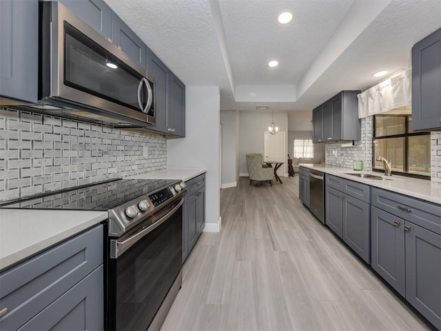 kitchen with appliances with stainless steel finishes, a textured ceiling, sink, decorative light fixtures, and light hardwood / wood-style floors