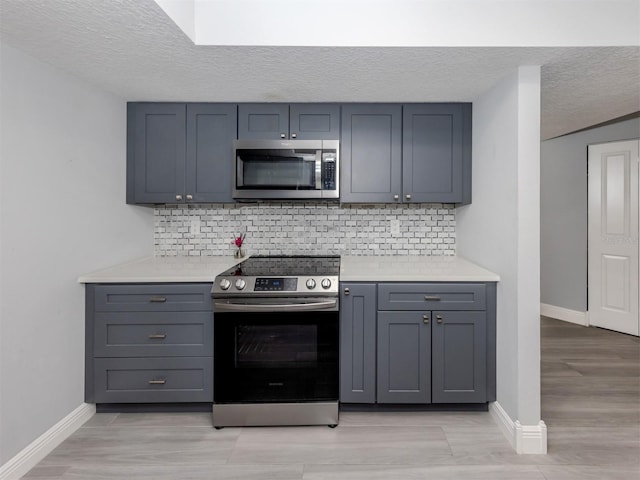 kitchen featuring gray cabinetry, decorative backsplash, stainless steel appliances, and a textured ceiling