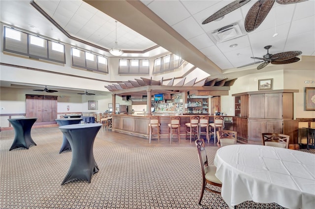 carpeted dining room with bar area, ceiling fan, and a towering ceiling