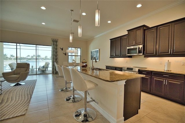 kitchen with sink, an island with sink, decorative light fixtures, light stone counters, and stainless steel appliances