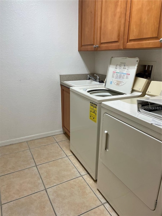 clothes washing area featuring washing machine and clothes dryer, sink, light tile patterned floors, and cabinets