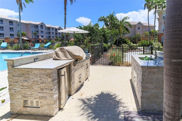 view of patio / terrace featuring an outdoor kitchen, sink, grilling area, and a community pool