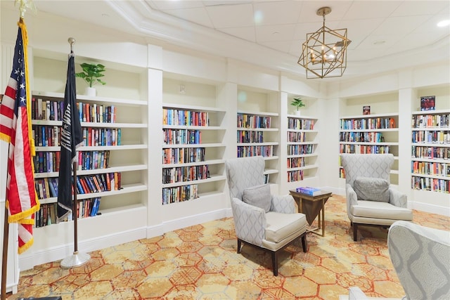 sitting room featuring built in shelves, crown molding, and a notable chandelier