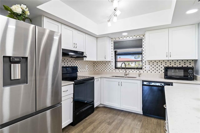 kitchen with a tray ceiling, sink, white cabinets, and black appliances