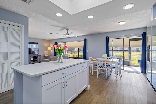 kitchen with ceiling fan, a kitchen island, wood-type flooring, a textured ceiling, and white cabinets