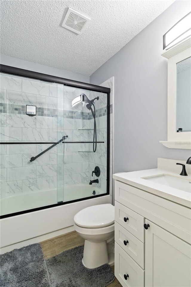 full bathroom with hardwood / wood-style floors, bath / shower combo with glass door, a textured ceiling, toilet, and vanity