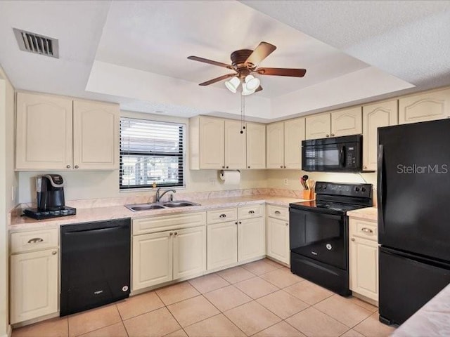 kitchen with black appliances, a raised ceiling, sink, light tile patterned floors, and cream cabinetry