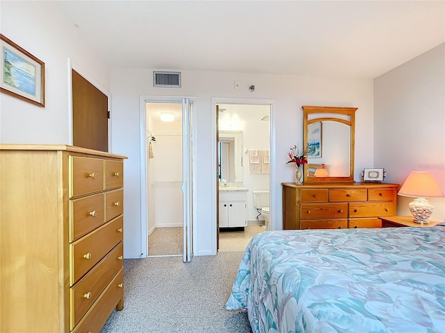 bedroom featuring ensuite bath, a walk in closet, a closet, and light colored carpet